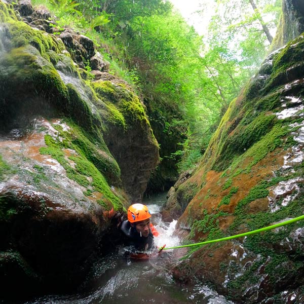 Barranquista descendiendo por una cuerda dentro del río mientras hace barranquismo en Asturias