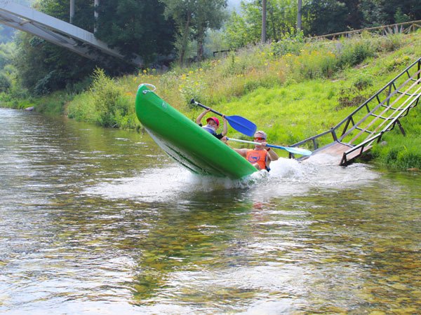 Padre con niño en una canoa entrando en el río después de bajar por la rampa de salida en la empresa Aipol aventura