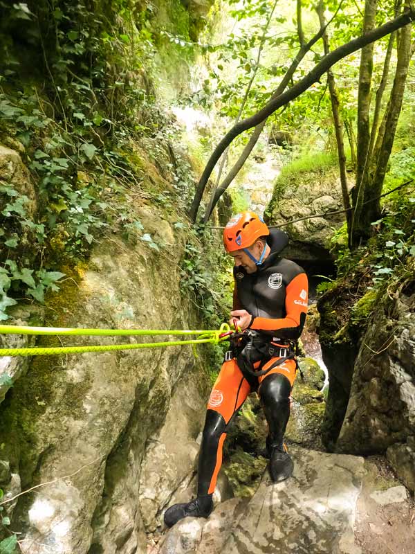 Un aventurero bajando por una cuerda rapelando una pared mientras hace barranquismo en Asturias,