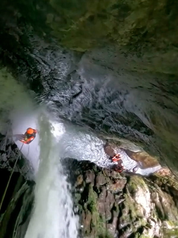 Haciendo rápel en pared junto a cascada de agua saliendo de la roca