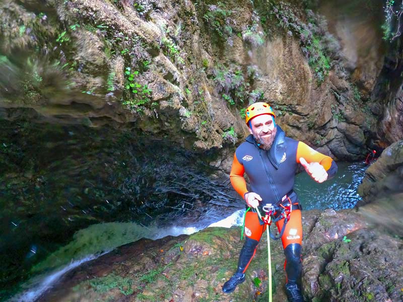 Barranquista con equipo de seguridad haciendo rapel en pared en el río