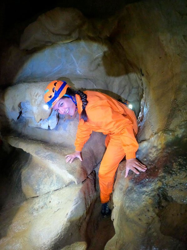 Mujer haciendo espeleología saliendo por hueco de cueva en Asturias